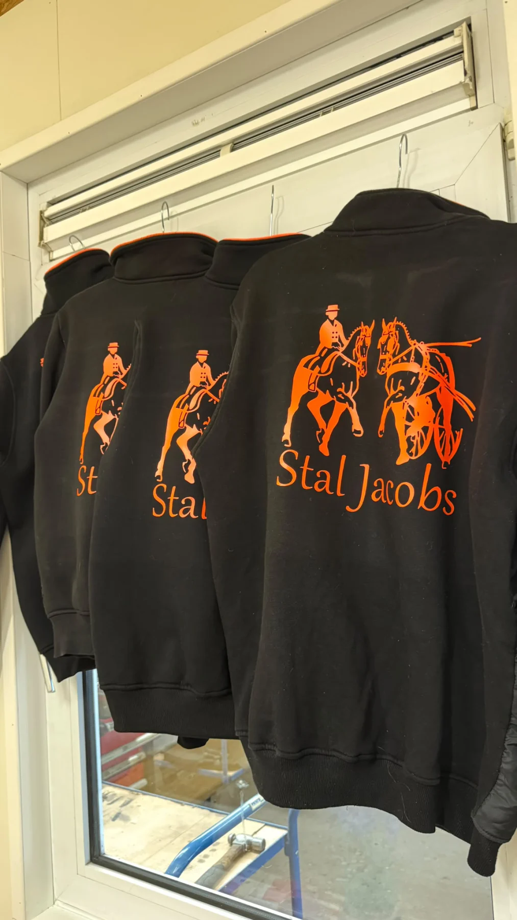 Zwarte hoodies met oranje paardenillustratie en de tekst Stal Jacobs
