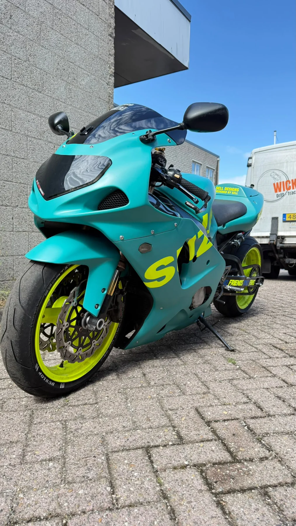 Turquoise motor met felgele letters en velgen, schuin van voren