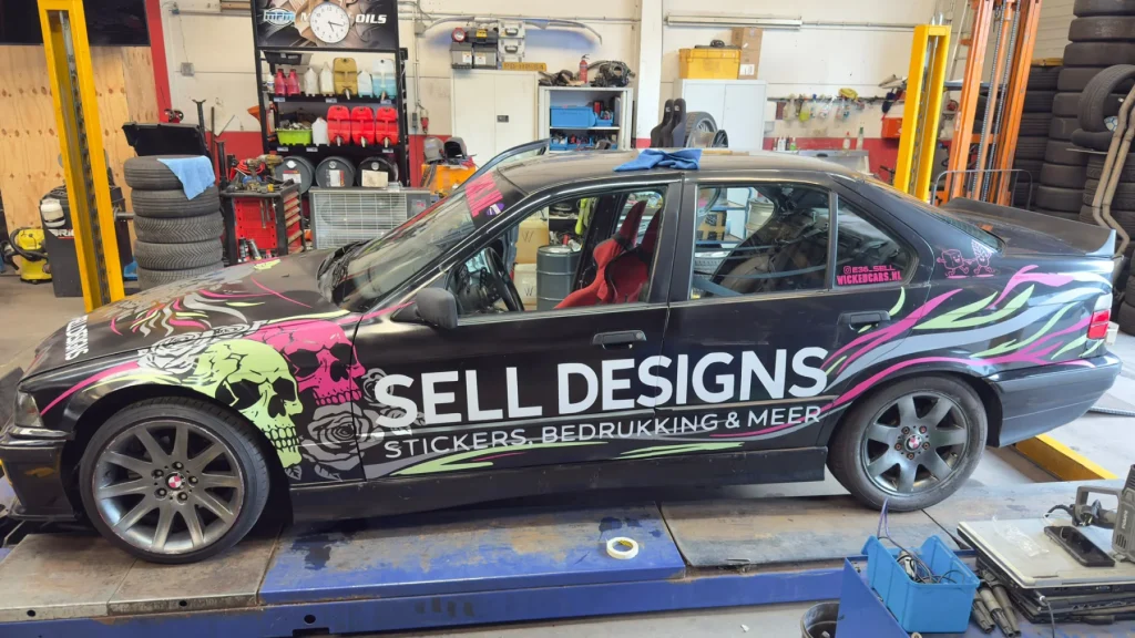 Sell Designs-auto met roze, groene en witte belettering op de zijkant