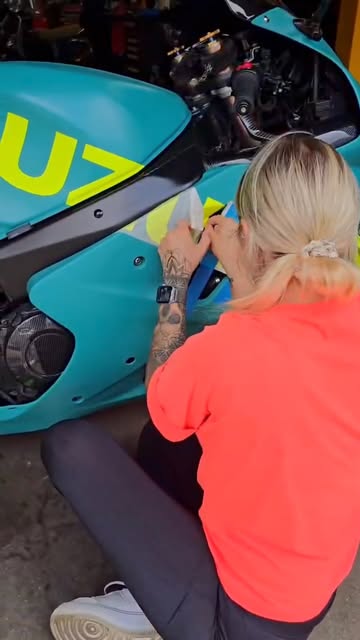 Selma brengt felgroene belettering aan op een turquoise motor