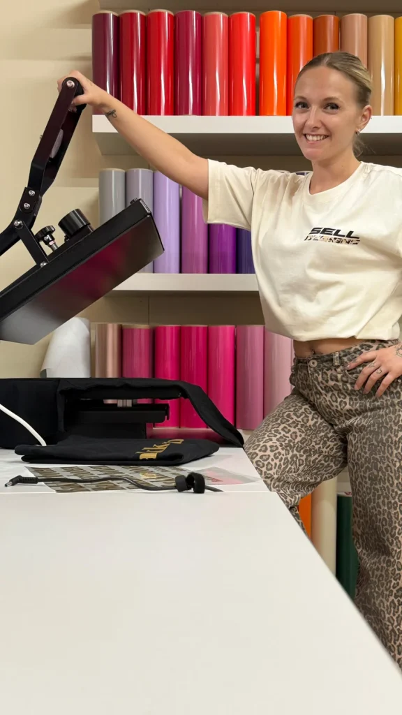 Selma met blond haar bij de kledingpers in de Sell Designs-werkplaats