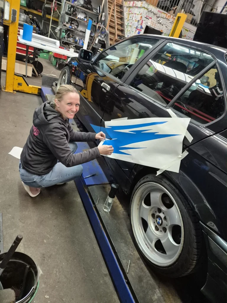 Selma werkt aan de belettering op de zijkant van een zwarte auto