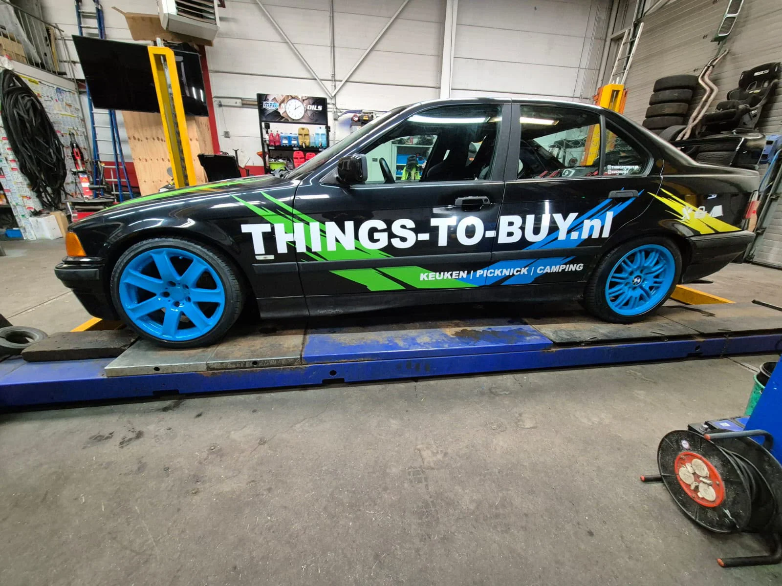Zwarte Things-To-Buy-auto met witte belettering, groen detail en blauwe velgen
