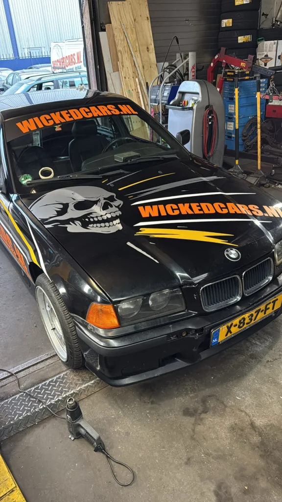 Zwarte Wickedcars-auto met oranje belettering op motorkap en voorruit