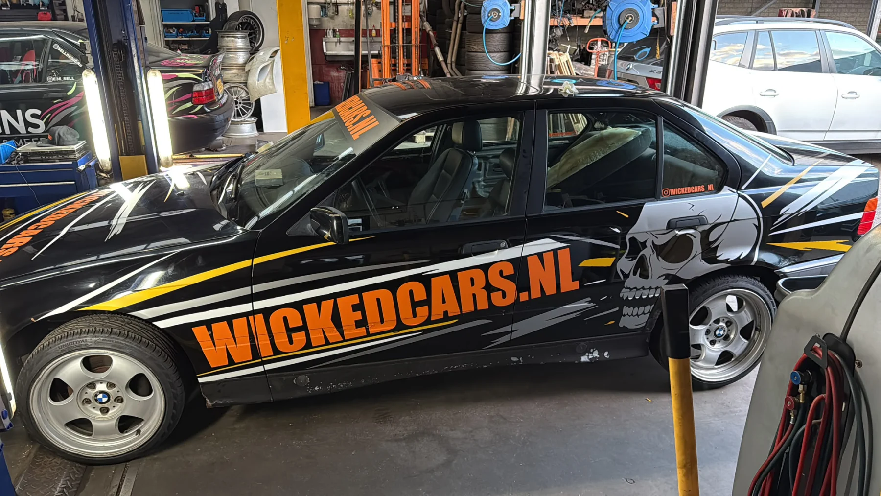 Zwarte auto met grote oranje Wickedcars.nl-belettering op de zijkant