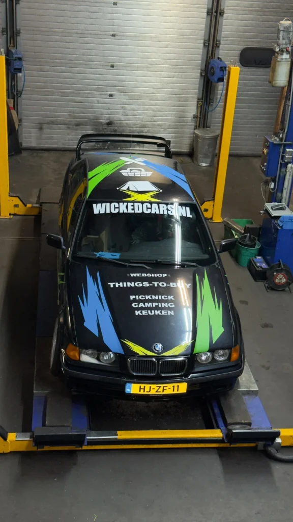 Wickedcars-auto in de werkplaats met blauwe en groene vlakken op de motorkap